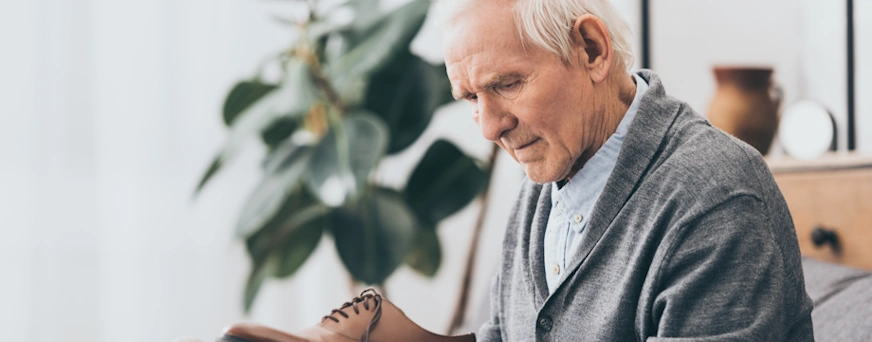 Life Assure Senior Man Holding shoes While Sitting On Sofa Hero